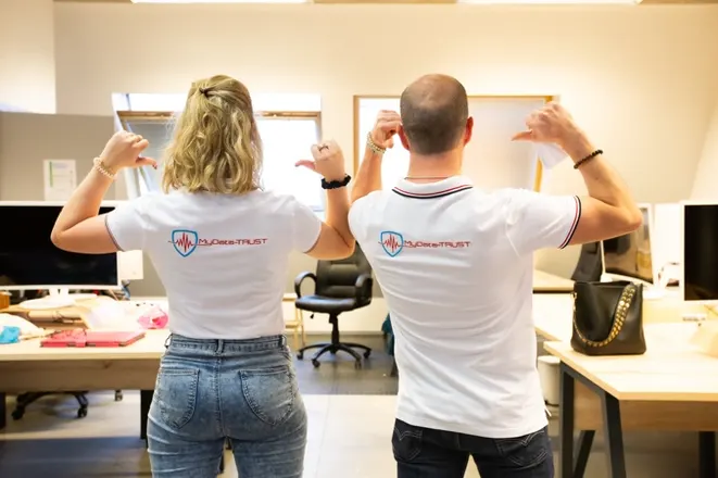 Two MyData-TRUST colleagues showing the logo on the back of their polo shirts in the office